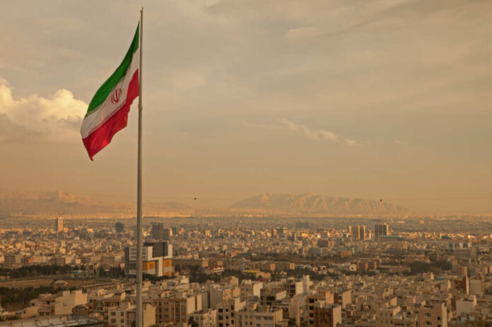 Iran,Flag,Waving,In,The,Wind,Above,Skyline,Of,Tehran