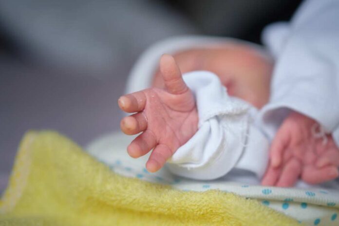 The,Newborn,Baby's,Hand,Reaches,Out,As,If,Trying,To