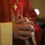 A close-up of a priests hands clasped together, wearing red vestments