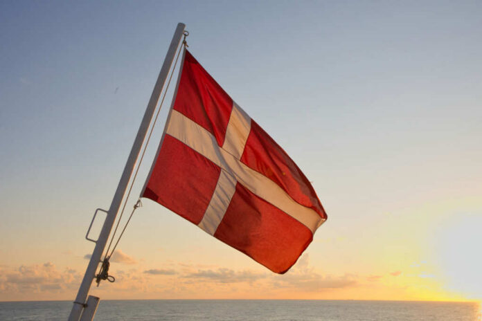 Danish flag waving against a sunset over the ocean