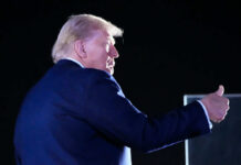 A political figure giving a thumbs up gesture at a night event