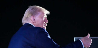 A political figure giving a thumbs up gesture at a night event