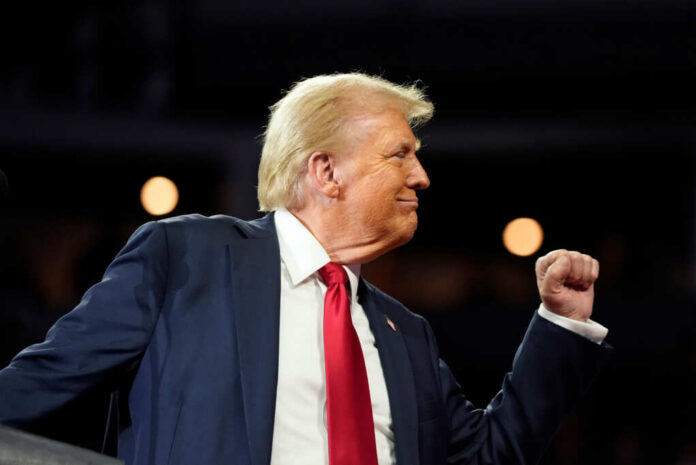 A man in a suit making a celebratory gesture during a speech
