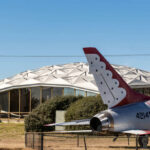 A military jet displayed in front of a modern geodesic dome structure