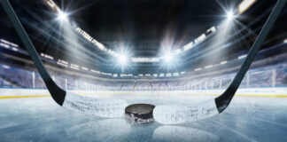 Close-up of a hockey puck on the ice with a hockey stick in the foreground