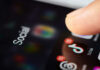 Close-up of a finger tapping a TikTok icon on a smartphone screen with social media labels
