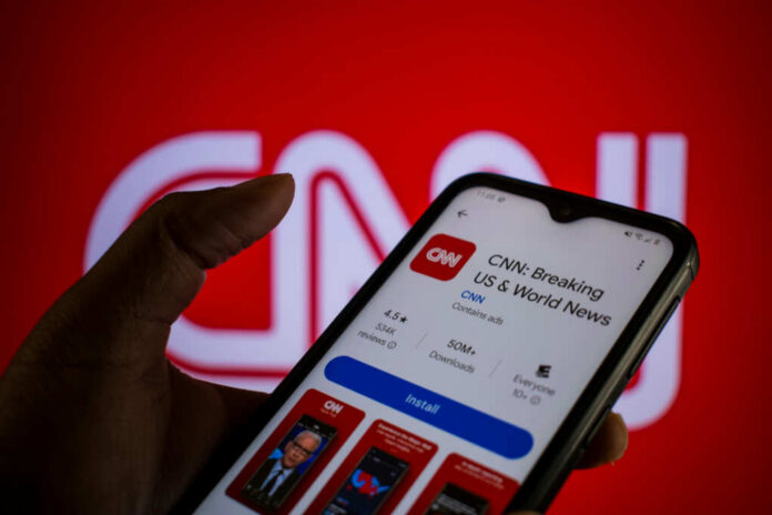 A hand holding a smartphone displaying the CNN news app against a red background