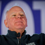 Man in a dark jacket speaking passionately at a podium with a microphone