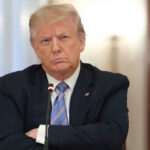 A serious-looking man in a suit with arms crossed during a meeting