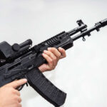 Person holding an AK-47 rifle with a scope