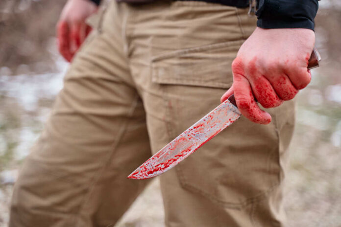 A person holding a bloody knife in an outdoor setting