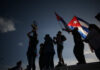 Silhouetted figures celebrating with a trophy and Cuban flags against a sunset sky