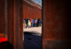 A line of people waiting near a border wall with barbed wire