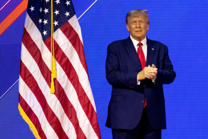 A man in a suit standing next to an American flag on stage