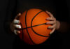 Hands with bandages holding an orange basketball against a dark background