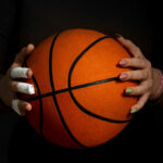 Hands with bandages holding an orange basketball against a dark background