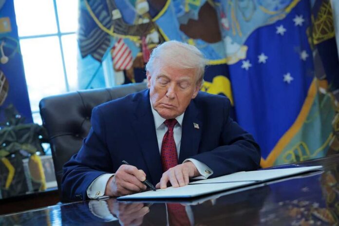 A person in a suit signing documents at a desk in the Oval Office