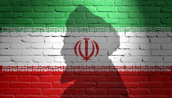 Silhouette of a figure against the Iranian flag painted on a brick wall