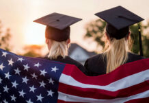 Two graduates wearing caps holding an American flag during sunset