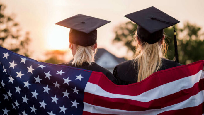 shutterstock1479083987jpg Two graduates wearing caps holding an American flag during sunset