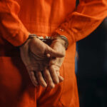 Individual in an orange jumpsuit with hands cuffed behind their back