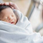 A newborn baby wrapped in a soft blanket, being cradled gently by an adult