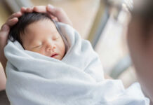 A newborn baby wrapped in a soft blanket, being cradled gently by an adult