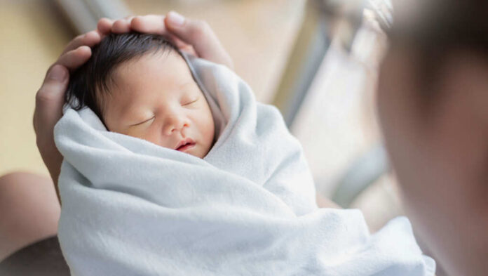 A newborn baby wrapped in a soft blanket, being cradled gently by an adult