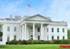 The White House with an American flag flying above, surrounded by greenery
