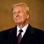 A man in formal attire smiling confidently against a neutral background