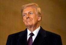 Trump’s Bold Blockade Stuns Iran A man in formal attire smiling confidently against a neutral background