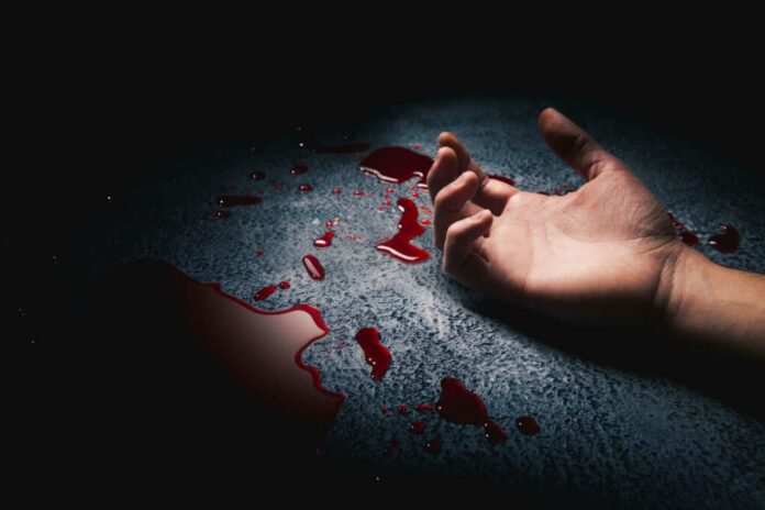 A hand lying on a surface with blood splatters around it