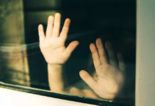 Child's hands pressed against a window, creating a reflective image