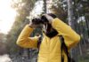 Person in a yellow jacket using binoculars in a forest