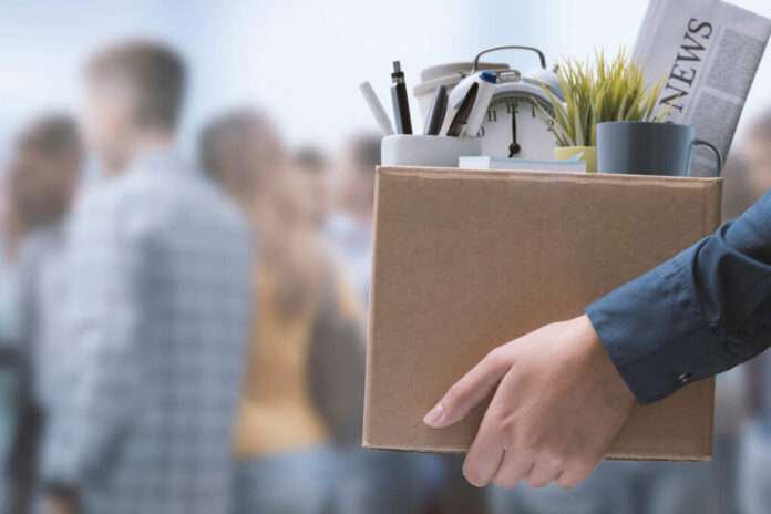 shutterstock_2157465795.jpg A person holding a cardboard box filled with office supplies and a newspaper