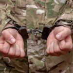 Person in military uniform with hands cuffed together