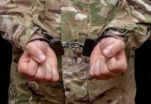 Person in military uniform with hands cuffed together