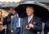 A man in formal attire holding an umbrella in the rain