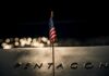 A small American flag positioned in front of the word 'PENTAGON' on a reflective surface
