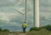 A worker in a yellow jacket walking among wind turbines