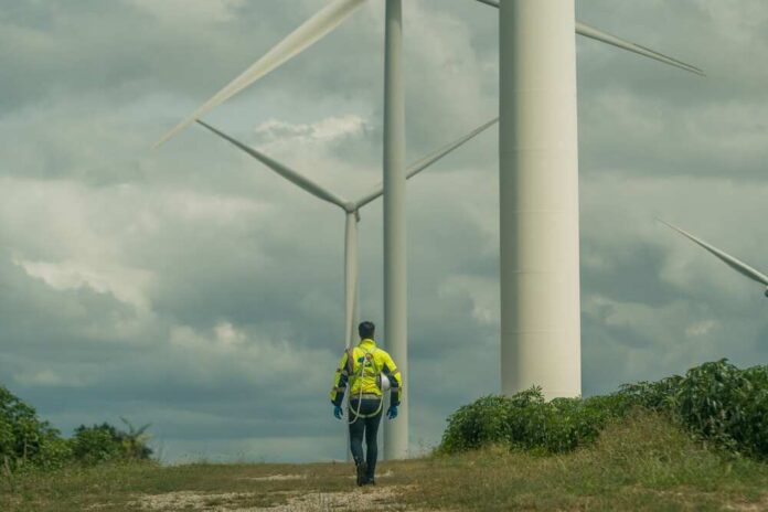 A worker in a yellow jacket walking among wind turbines