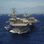 An aircraft carrier surrounded by various naval ships in the ocean