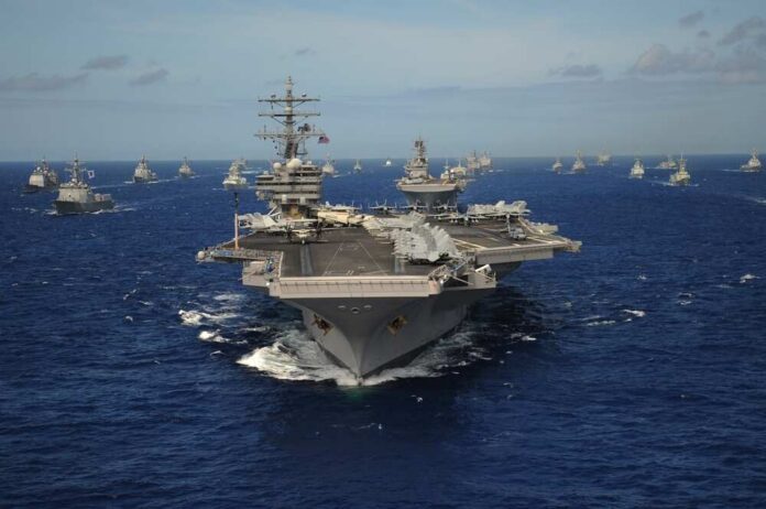 An aircraft carrier surrounded by various naval ships in the ocean