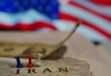 Map of Iran with push pins and a dollar bill in front of an American flag