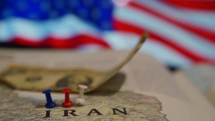 Map of Iran with push pins and a dollar bill in front of an American flag