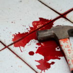 A bloody hammer resting on a tiled floor with red stains