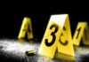 Yellow evidence markers with numbers at a crime scene alongside a bullet casing