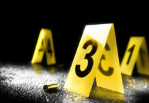 Yellow evidence markers with numbers at a crime scene alongside a bullet casing