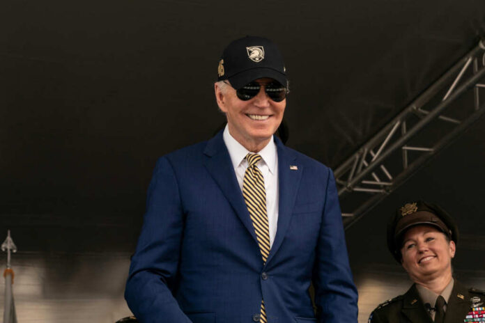 A smiling man in a suit and sunglasses at a military event, with a woman in uniform beside him
