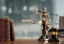 A bronze statue of Lady Justice holding scales and a sword, with law books and a gavel in the foreground
